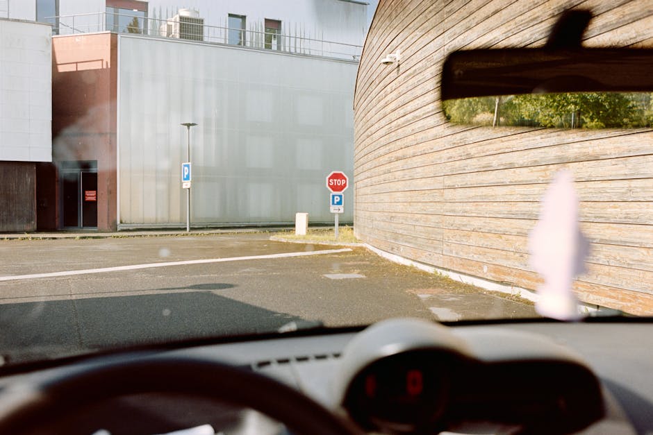 View from inside a parked car at a street intersection with stop and parking signs visible.